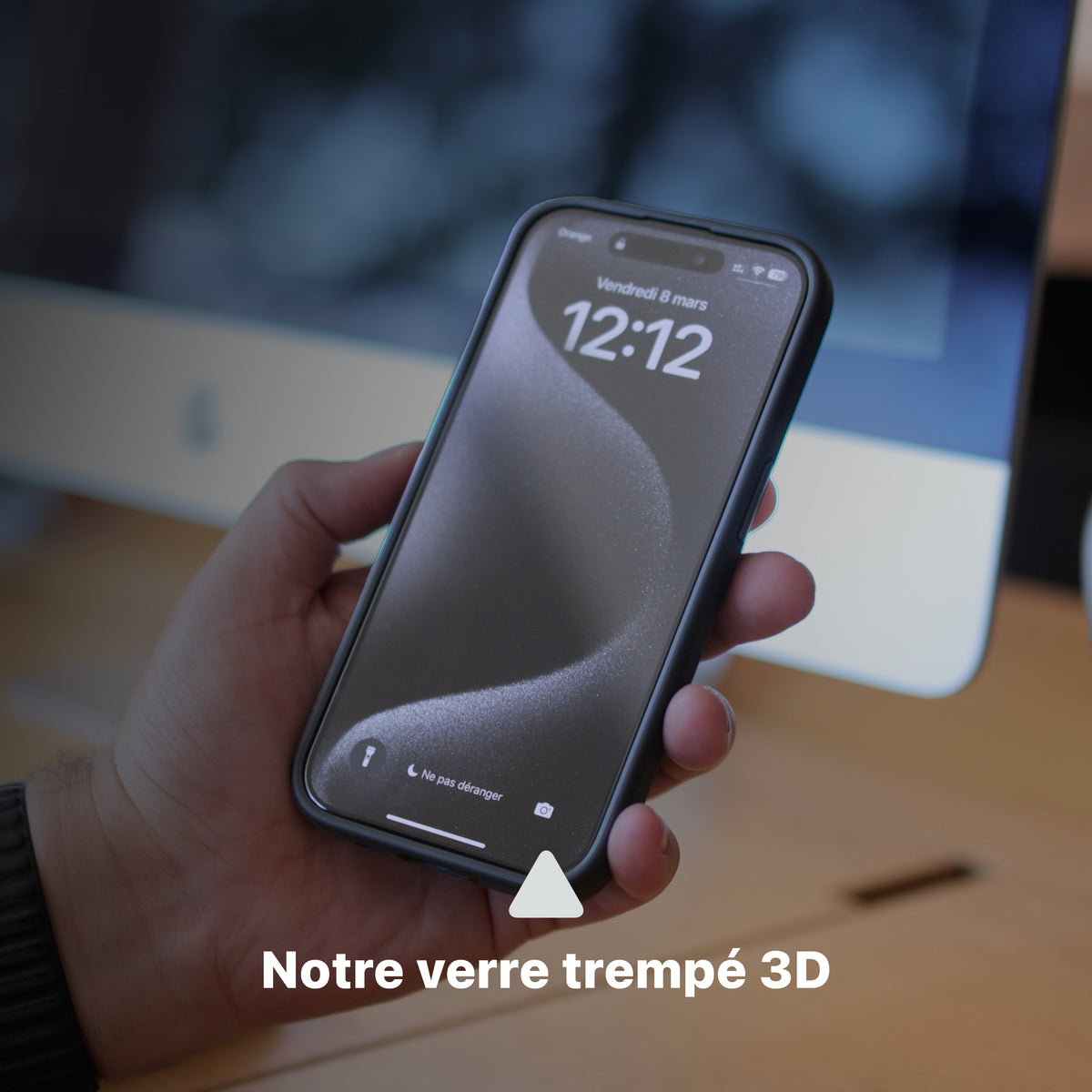 Téléphone en coque ONE noire tenu en main devant un ordinateur, avec mise en avant du verre trempé 3D