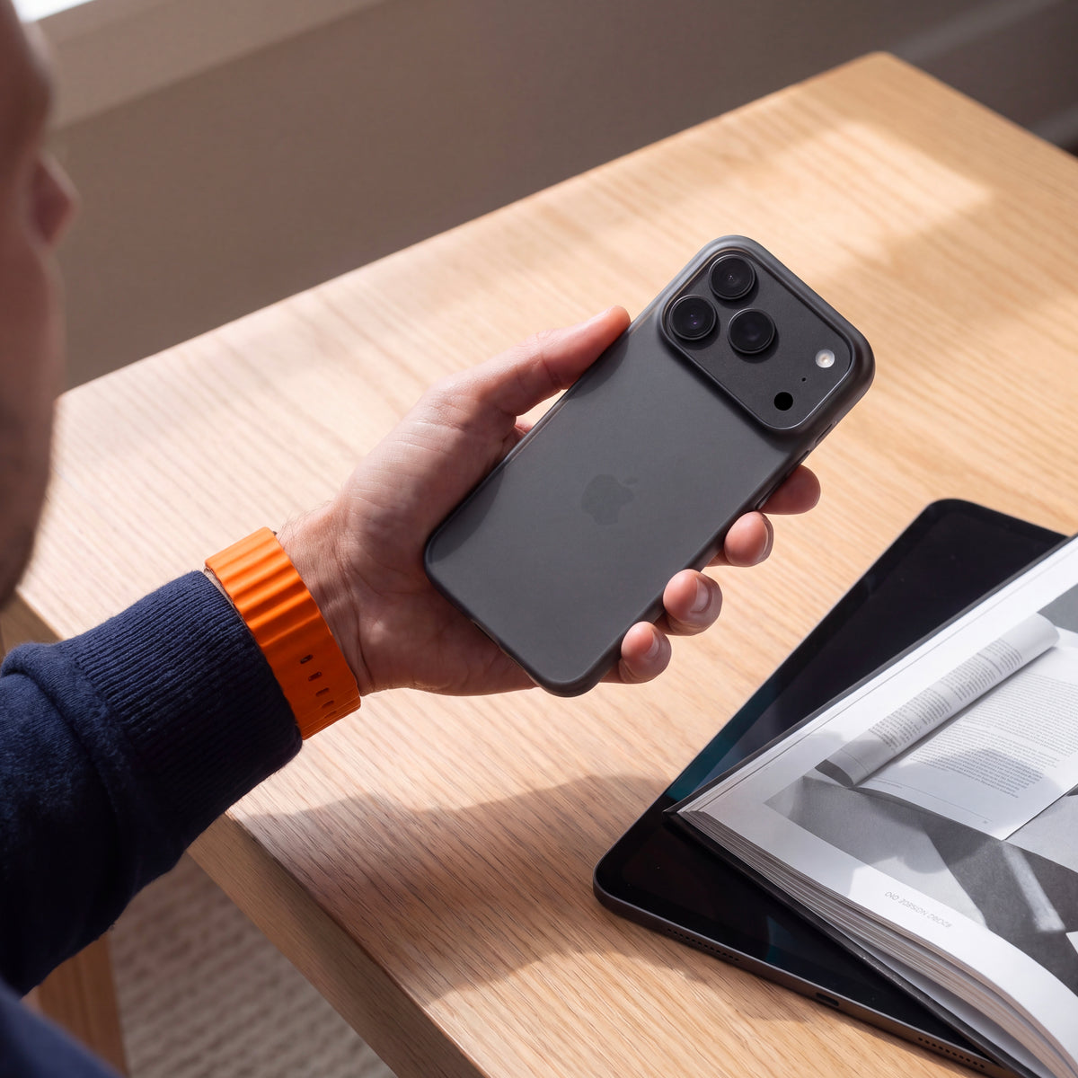 Coque ORIGINAL Noir fumé sur iPhone 18 Pro et Pro Max, tenue en main au-dessus d’une table en bois