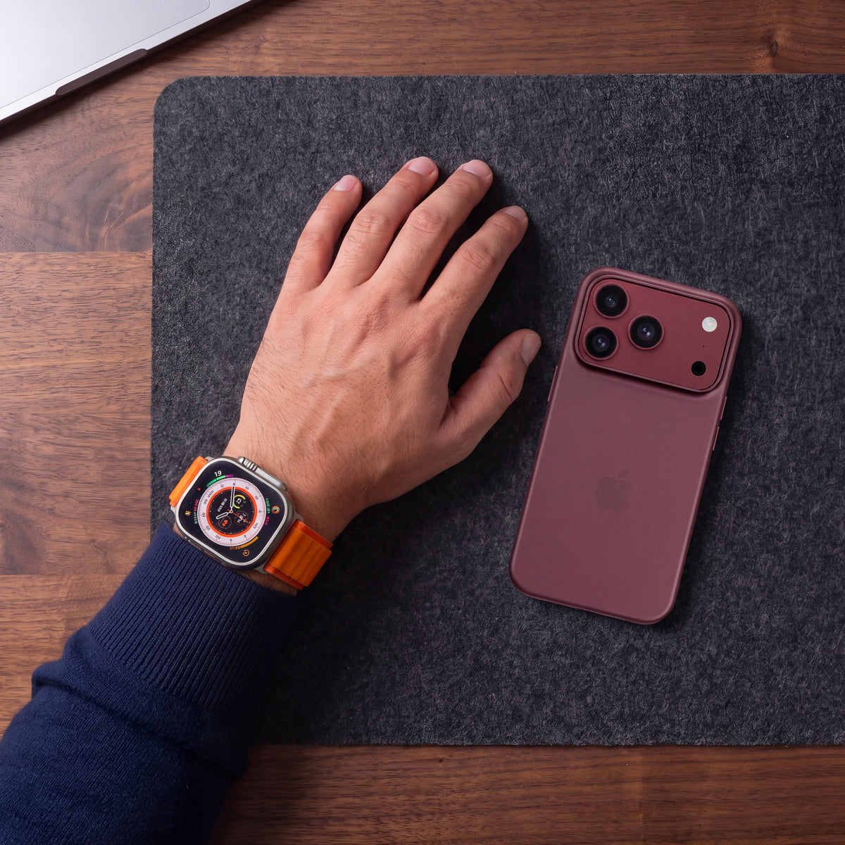 iPhone en coque ORIGINAL Bordeaux posé sur un tapis de bureau en feutre, à côté d’une main