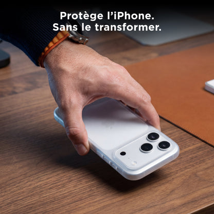 Une main saisit un iPhone équipé de la coque PHANTOM transparente sur un bureau en bois
