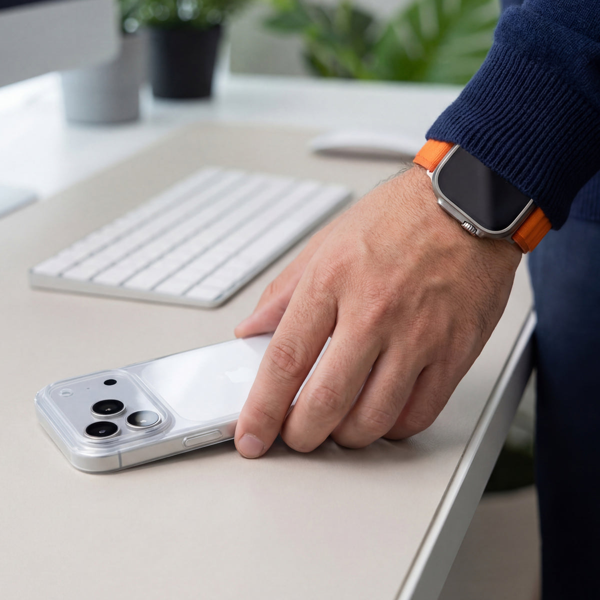 Une main pose un iPhone en coque PHANTOM transparente sur un bureau clair