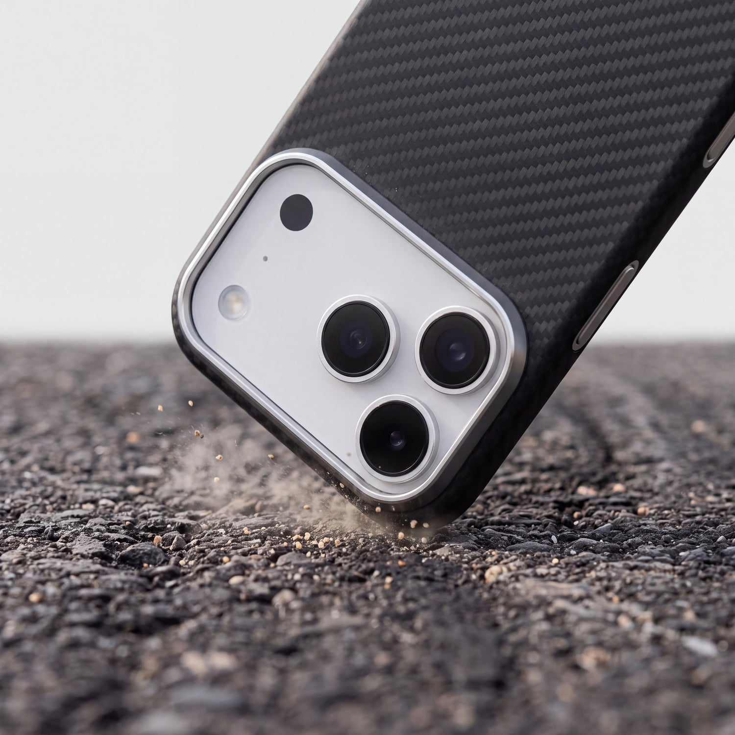 Téléphone en coque CARBON heurtant l'asphalte par un angle, fine poussière soulevée au point d'impact