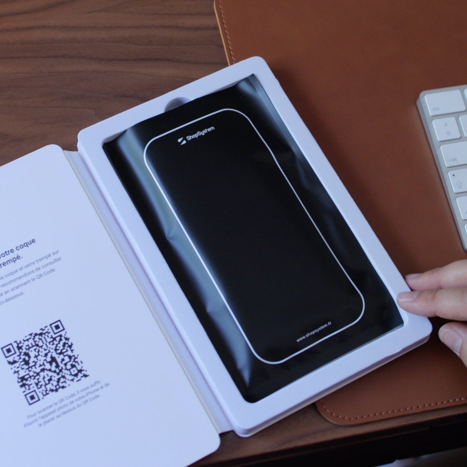 Coque dans son emballage ouvert sur un sous-main en cuir, notice d'installation et QR code visibles