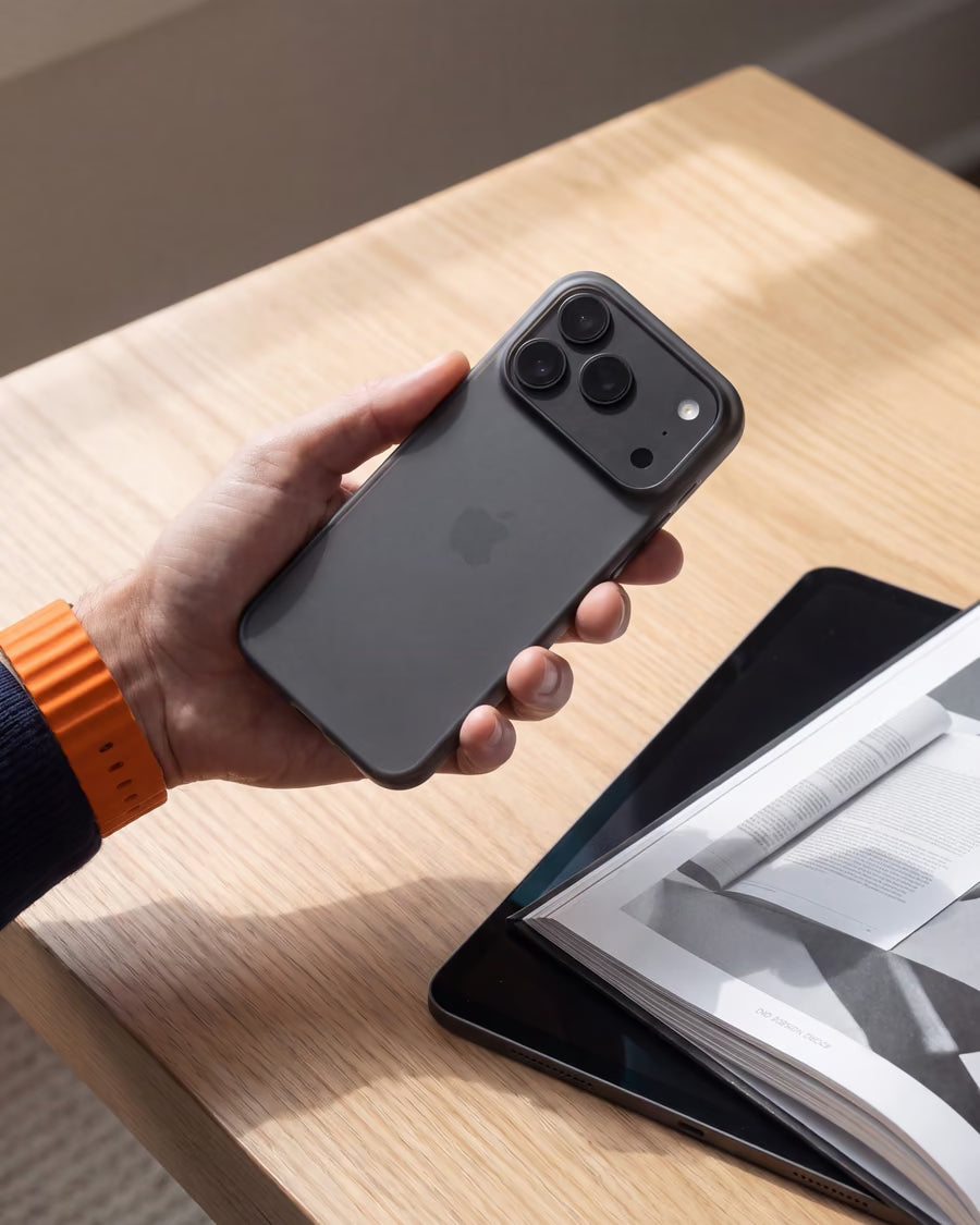 Une main tient un iPhone dans une coque ORIGINAL Noir fumé au-dessus d'un bureau