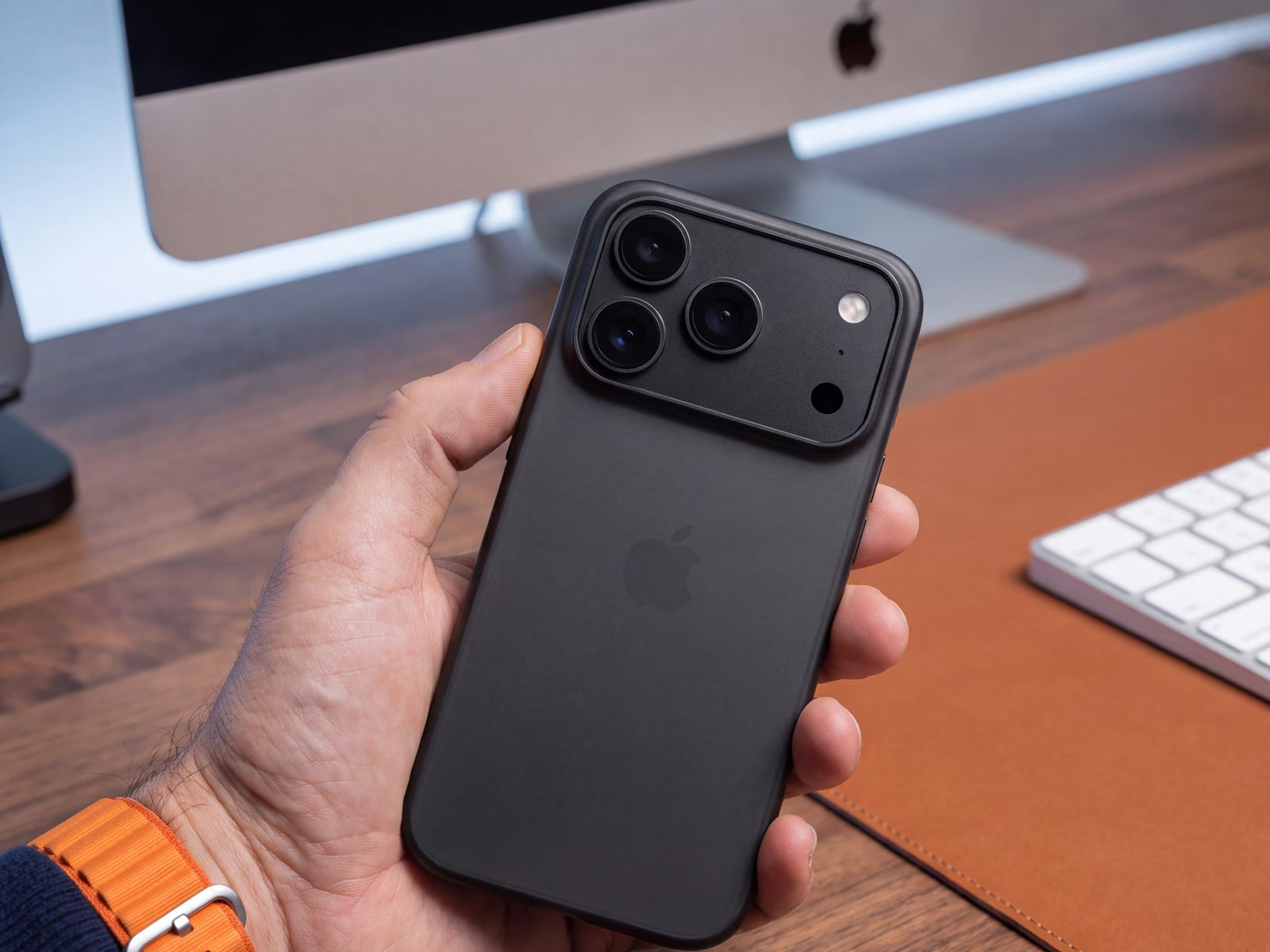 Une main tient un iPhone 18 Pro dans une coque ORIGINAL Noir fumé devant un bureau